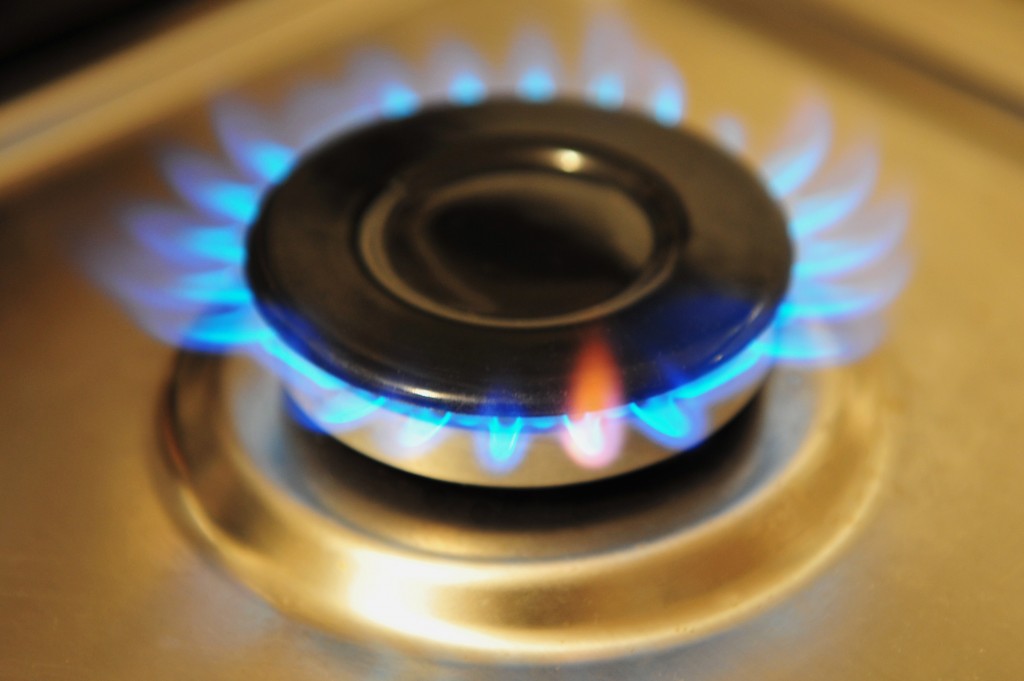 Stainless steel gas burner turned on with blue gas flame.