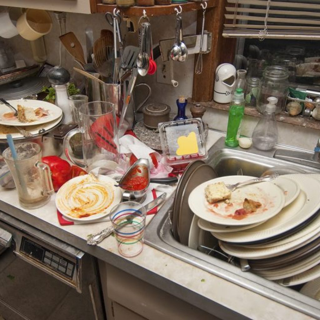Broken dishwasher causing piled up dirty dishes in the sink, showing the need for the best dishwasher repair service at home.