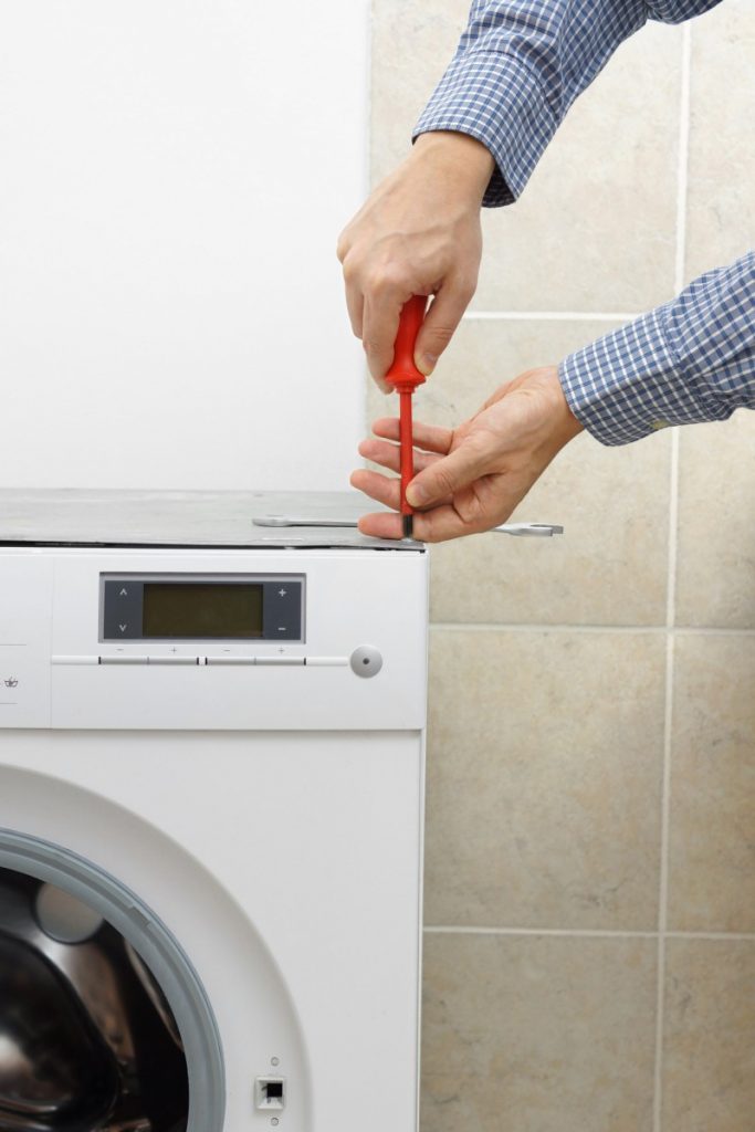 Technician servicing washing machine with screwdriver, ensuring proper appliance maintenance
