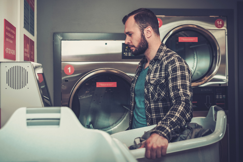 Handsome man doing laundry at laundromat shop. | All Area Appliance