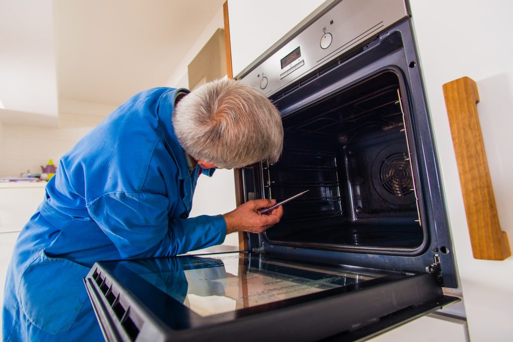 Professional handyman performing oven repair on a kitchen oven by inspecting and fixing internal components.