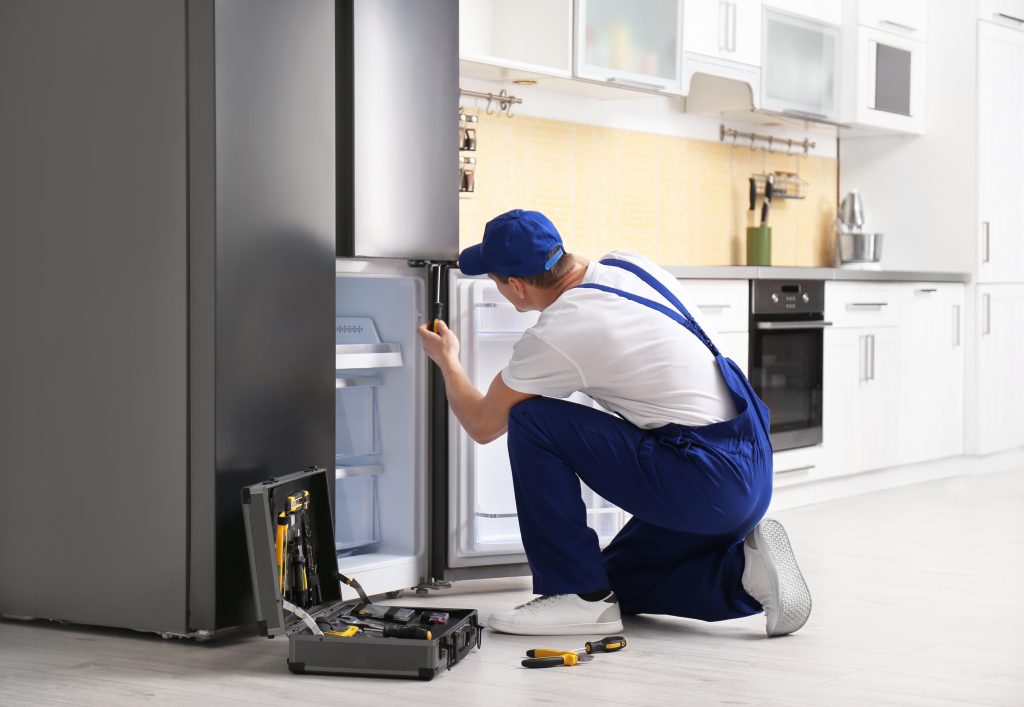 Male technician with screwdriver performing reliable appliance repair on a refrigerator in a modern kitchen.