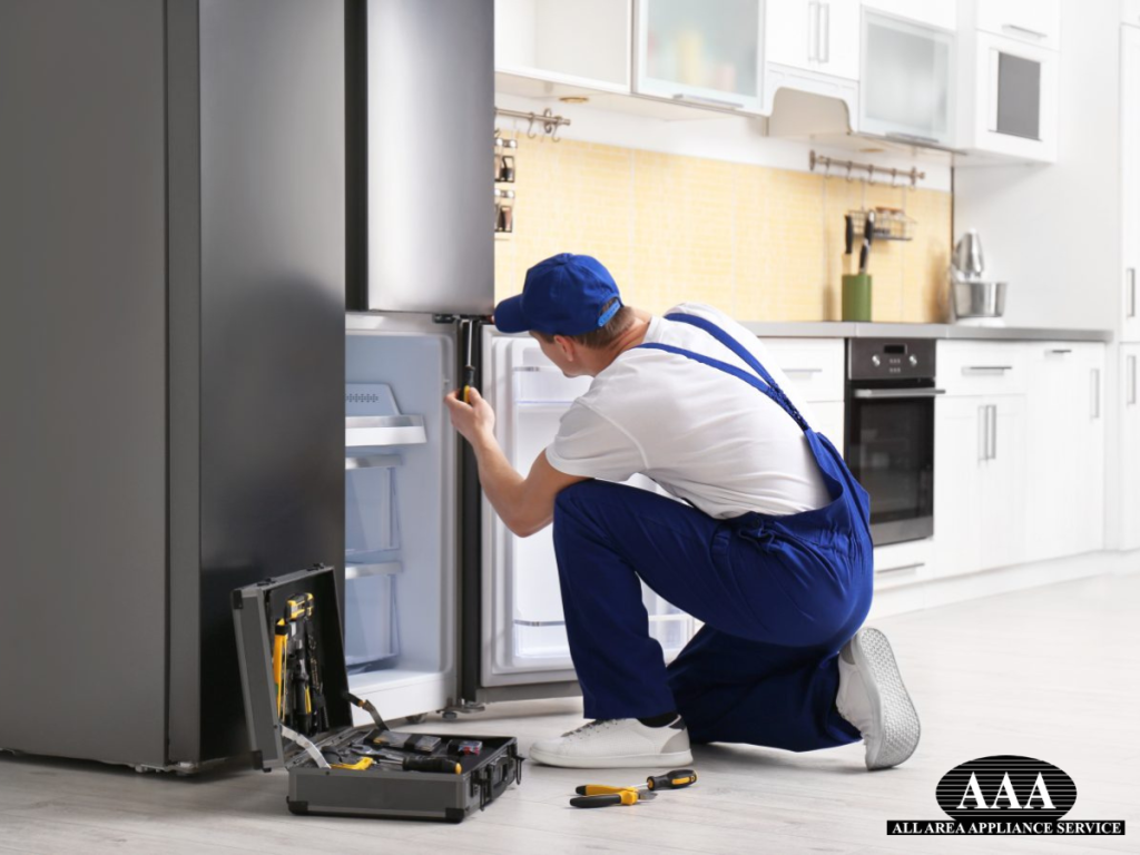Male technician with screwdriver performing reliable appliance repair on a refrigerator in a modern kitchen.