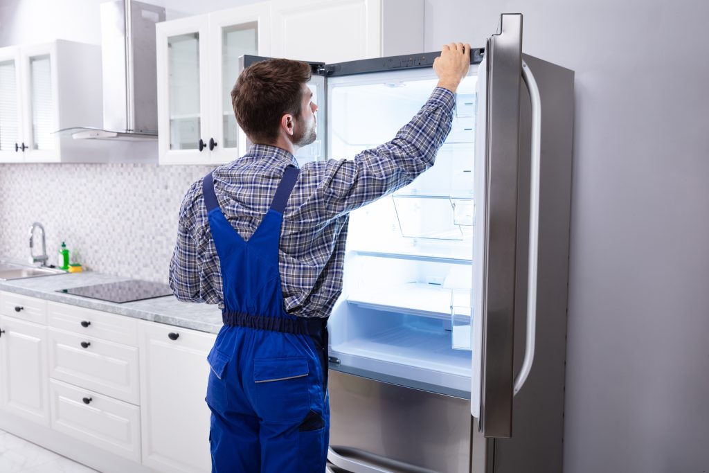 Serviceman checking refrigerator temperature in a kitchen as part of professional freezer repair to detect hidden issues.